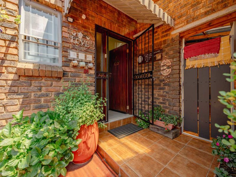 A welcoming townhouse entrance featuring a face brick facade, tiled porch, and a secure metal gate leading to a timber front door.