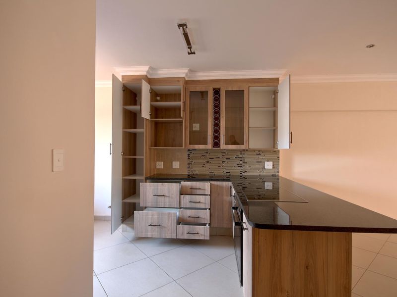 Modern kitchen featuring light wood-finish cabinetry, dark granite countertops, integrated hob and oven, and a decorative mosaic tile backsplash.