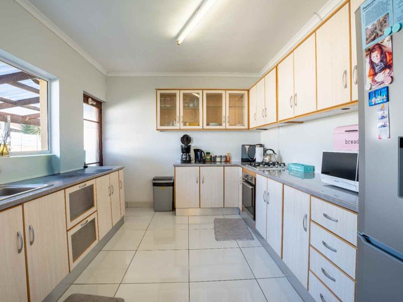 A functional kitchen featuring light-toned cabinetry, laminate countertops, a gas hob, built-in oven, and tiled flooring with ample natural light.