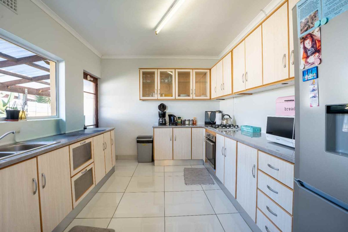 A functional kitchen featuring light-toned cabinetry, laminate countertops, a gas hob, built-in oven, and tiled flooring with ample natural light.