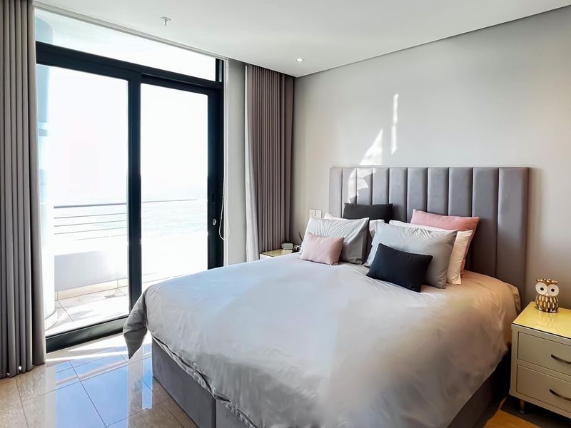 Modern bedroom featuring tiled flooring, recessed lighting, and a large sliding glass door providing access to a balcony with ocean views.