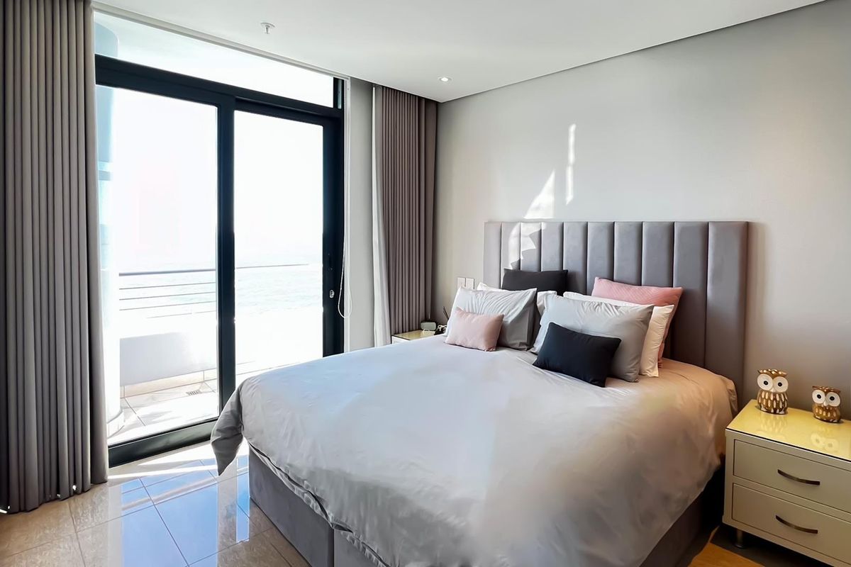 Modern bedroom featuring tiled flooring, recessed lighting, and a large sliding glass door providing access to a balcony with ocean views.