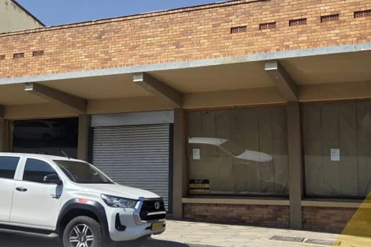 Front exterior view of a commercial property featuring a brick facade, large display windows, and a secure metal roller shutter entrance.