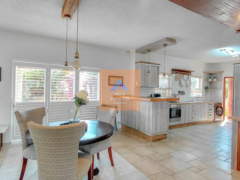 Open-plan living and kitchen area featuring modern cabinetry, a breakfast bar, subway tile backsplash, and direct access to the outdoor space via shuttered doors.