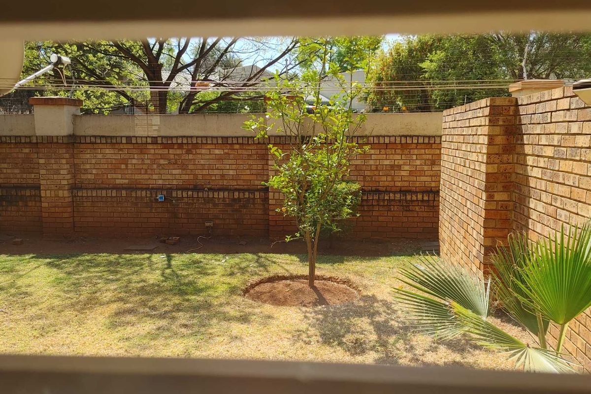 A private rear garden area featuring a brick boundary wall with electric fencing and a small established tree.