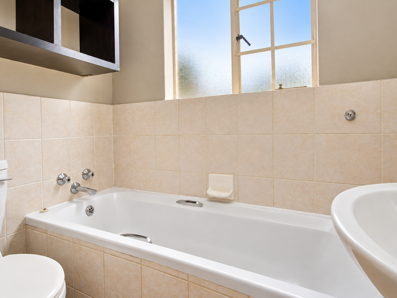 A functional bathroom featuring a standard bathtub, toilet, basin, and neutral wall tiling with a window for natural light.