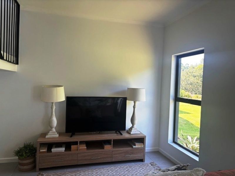 A bright living area featuring a modern staircase balustrade and a large window with views of the surrounding greenery.