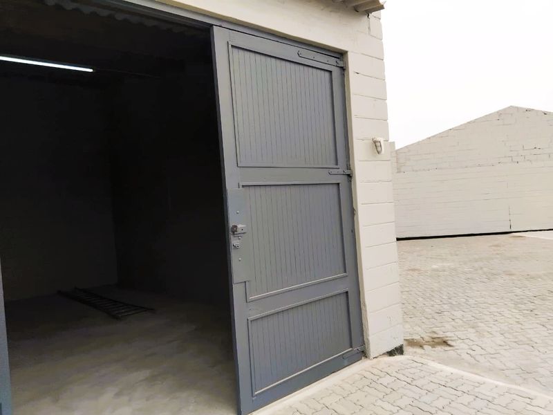 A functional industrial garage space featuring a sturdy hinged door, concrete block construction, and paved exterior access area.