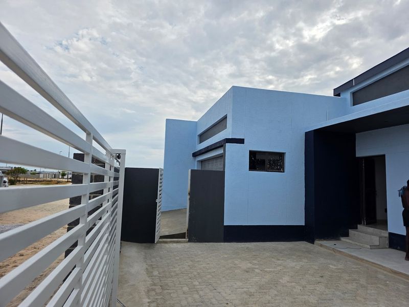 Modern exterior front facade featuring a paved driveway, metal gate, and contemporary blue and dark grey painted concrete walls.
