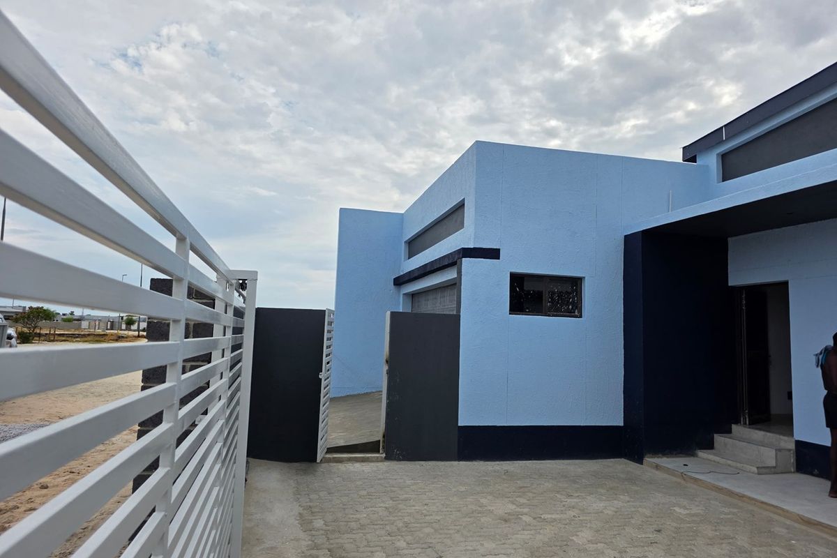 Modern exterior front facade featuring a paved driveway, metal gate, and contemporary blue and dark grey painted concrete walls.