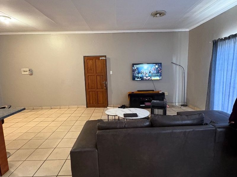 Open plan living area featuring tiled flooring, coved ceilings, and a solid timber door, providing a functional and spacious layout.