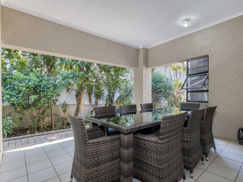 A covered patio area featuring tiled flooring, plastered walls, and a louvre window, providing a pleasant outdoor space overlooking the garden.