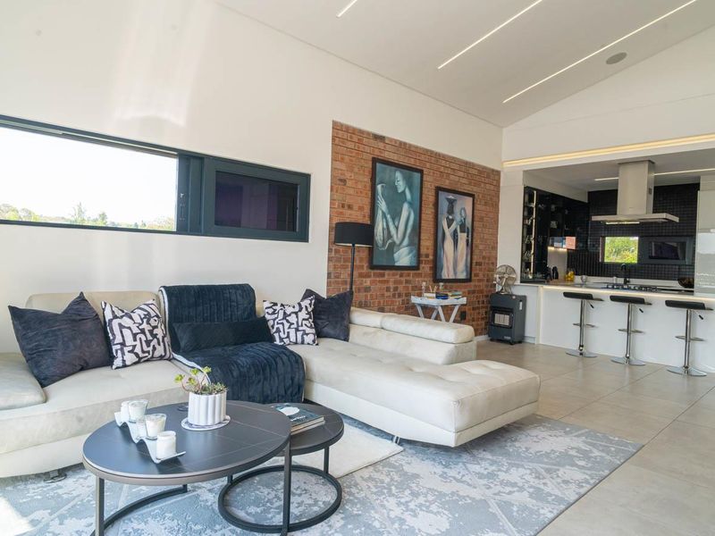 Modern open-plan living area featuring a striking exposed brick wall, sleek kitchen island with breakfast bar, and contemporary recessed linear ceiling lighting.