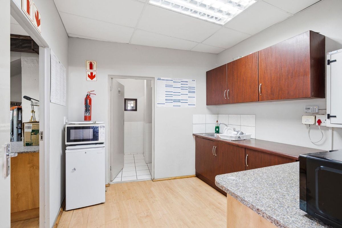 Functional kitchenette area featuring laminate cabinetry, durable countertops, stainless steel sink, and tiled splashback, with direct access to a secondary utility room.