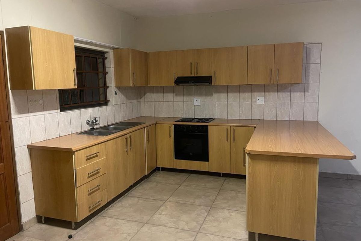 A functional U-shaped kitchen featuring light wood-look cabinetry, a built-in oven, hob, extractor fan, and a double sink with tiled backsplash.