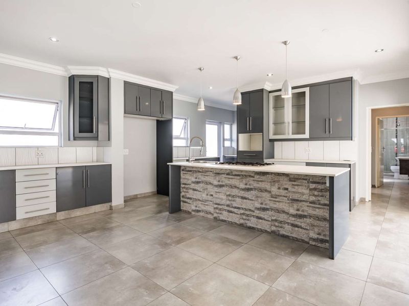 Modern kitchen featuring a central island with stone-cladding, sleek grey cabinetry, tiled flooring, and recessed lighting in an open-plan layout.