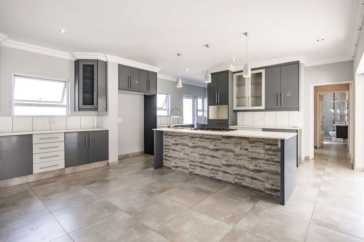 Modern kitchen featuring a central island with stone-cladding, sleek grey cabinetry, tiled flooring, and recessed lighting in an open-plan layout.