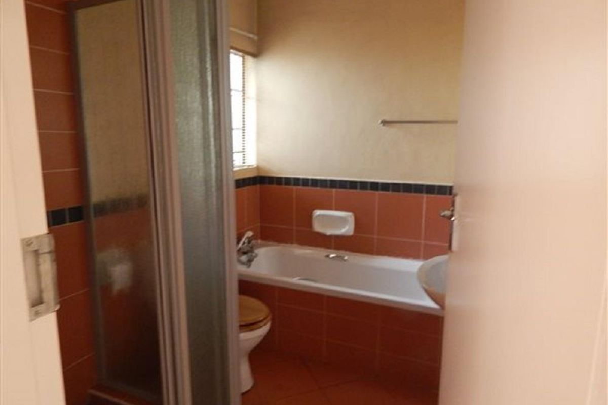 A dated bathroom featuring a built-in bathtub, a separate shower enclosure, and a pedestal basin with terracotta-toned wall and floor tiling.