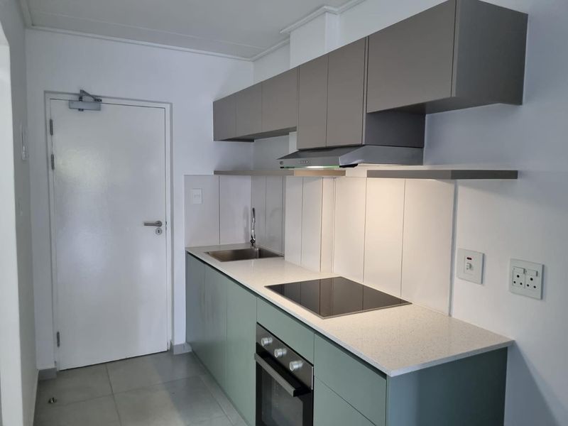 Modern kitchen featuring sage green lower cabinetry, grey upper cabinets, stone countertops, integrated electric hob, oven, and extractor fan with tiled flooring.
