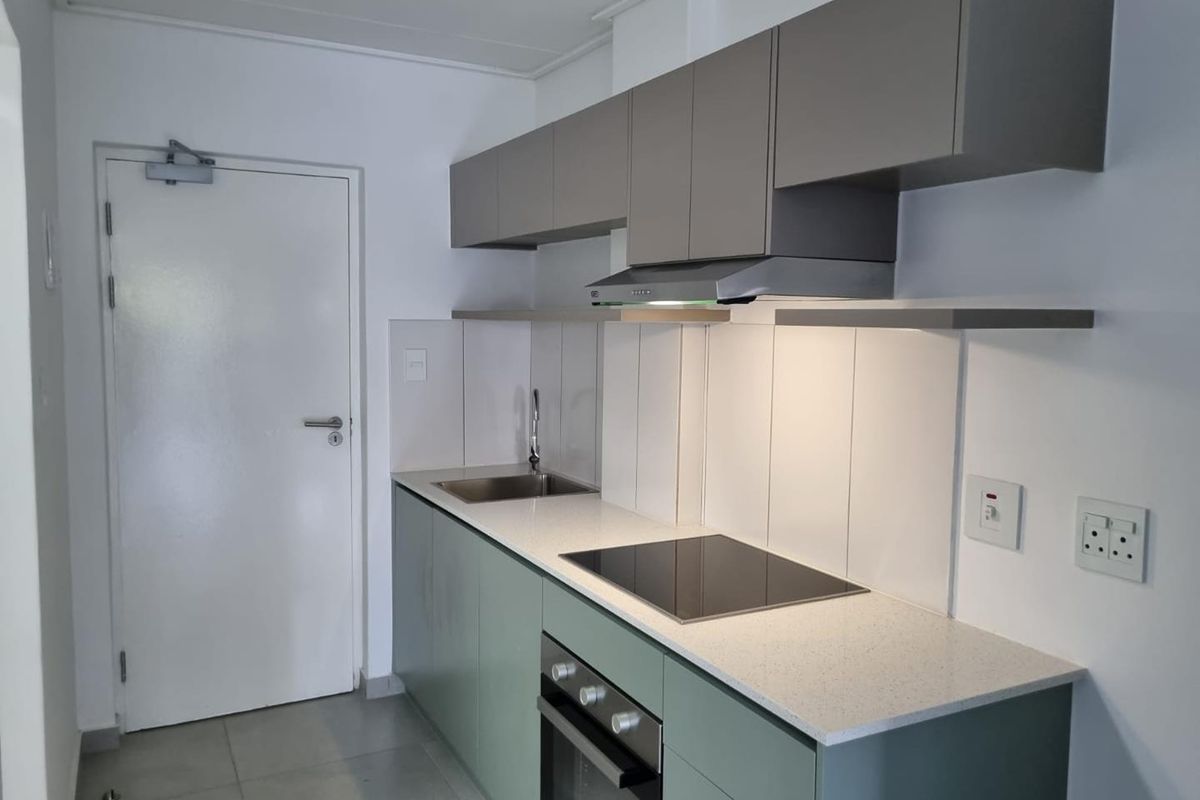 Modern kitchen featuring sage green lower cabinetry, grey upper cabinets, stone countertops, integrated electric hob, oven, and extractor fan with tiled flooring.