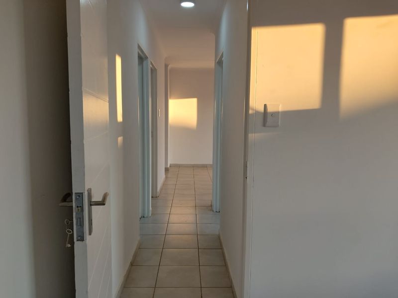 A clean, empty hallway featuring neutral tiled flooring and multiple internal door access points, illuminated by natural light.