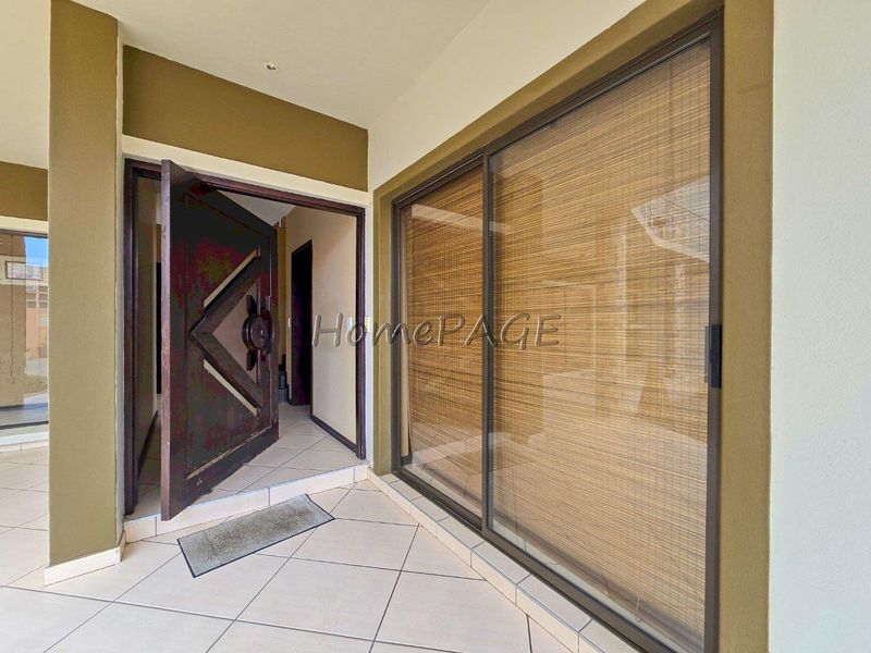 A covered patio area featuring tiled flooring, a large sliding glass door, and a decorative solid wood entrance door.