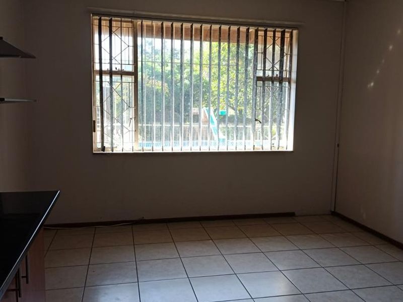 An empty kitchen area featuring tiled flooring, built-in cabinetry, and a window fitted with security bars.