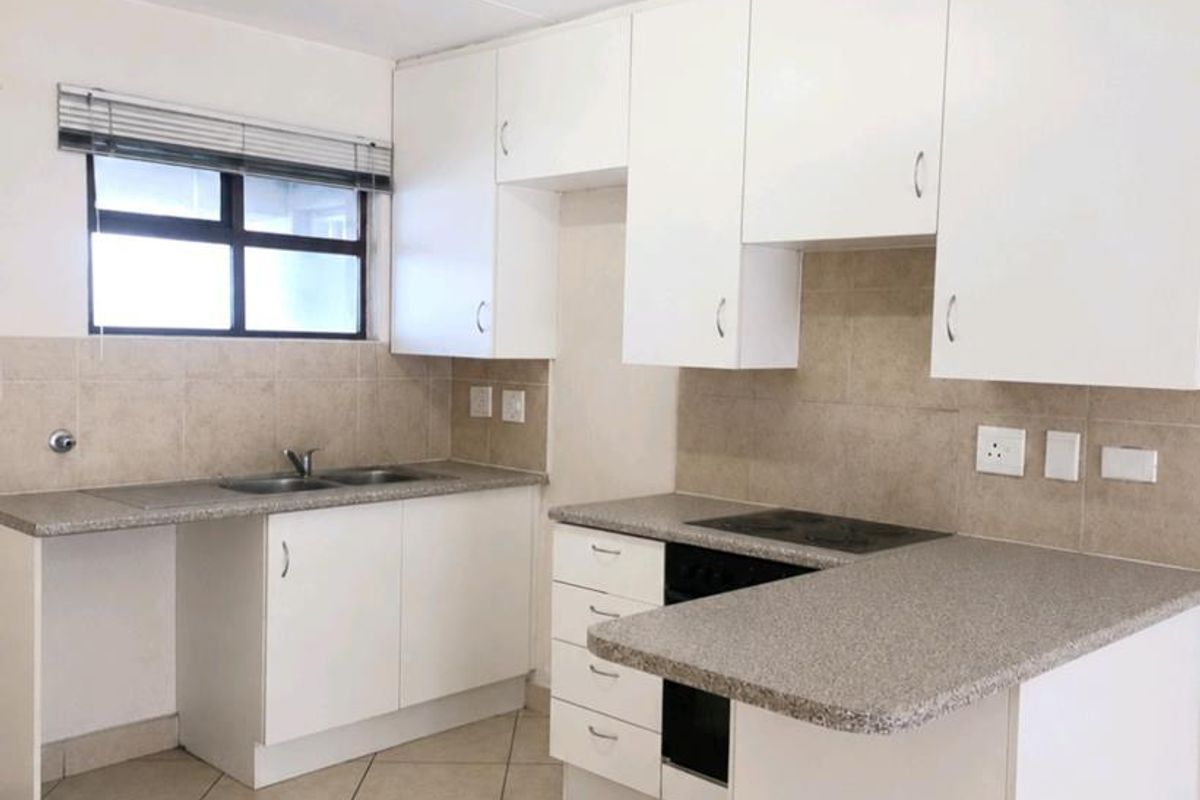 A clean, functional kitchen featuring white cabinetry, laminate countertops, a built-in oven and hob, and neutral ceramic tile flooring.
