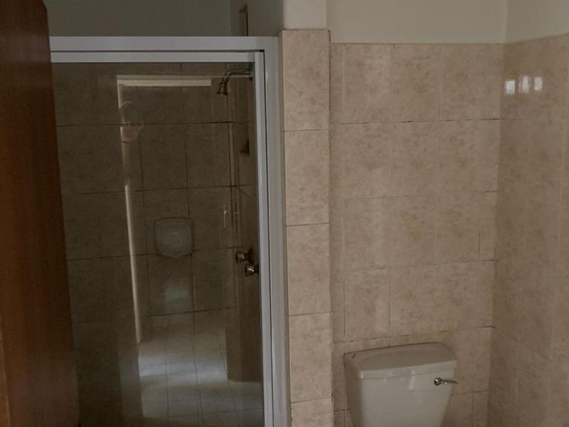 A functional bathroom featuring a glass-enclosed shower and a standard toilet with neutral ceramic wall and floor tiling.