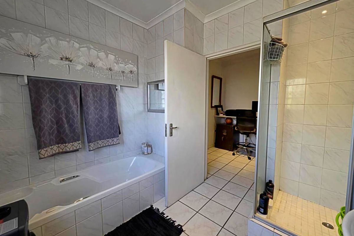 A functional bathroom featuring a built-in bathtub, a separate glass-enclosed shower, and full-height wall tiling, with direct access to an adjacent room.