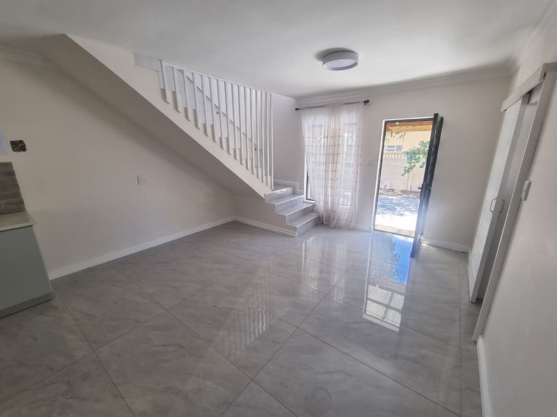 Bright open-plan living area featuring modern tiled flooring, a staircase with a white balustrade, and direct access to the outdoor space.
