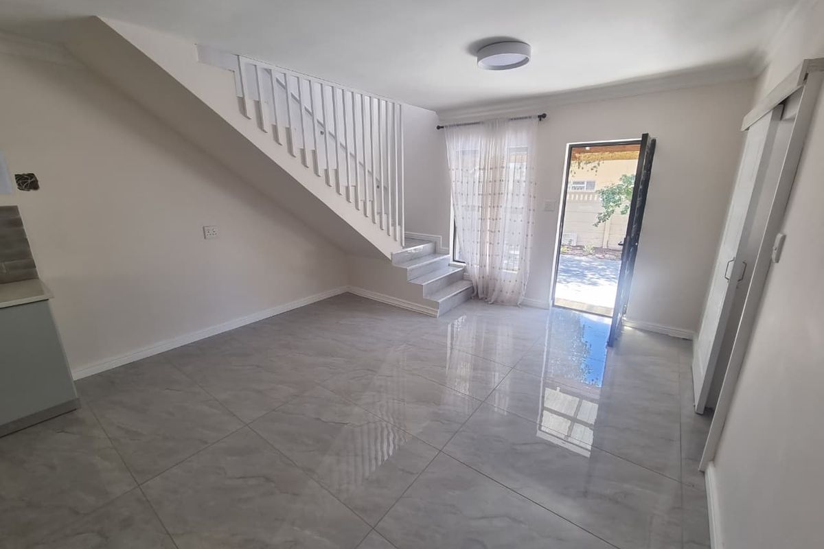 Bright open-plan living area featuring modern tiled flooring, a staircase with a white balustrade, and direct access to the outdoor space.