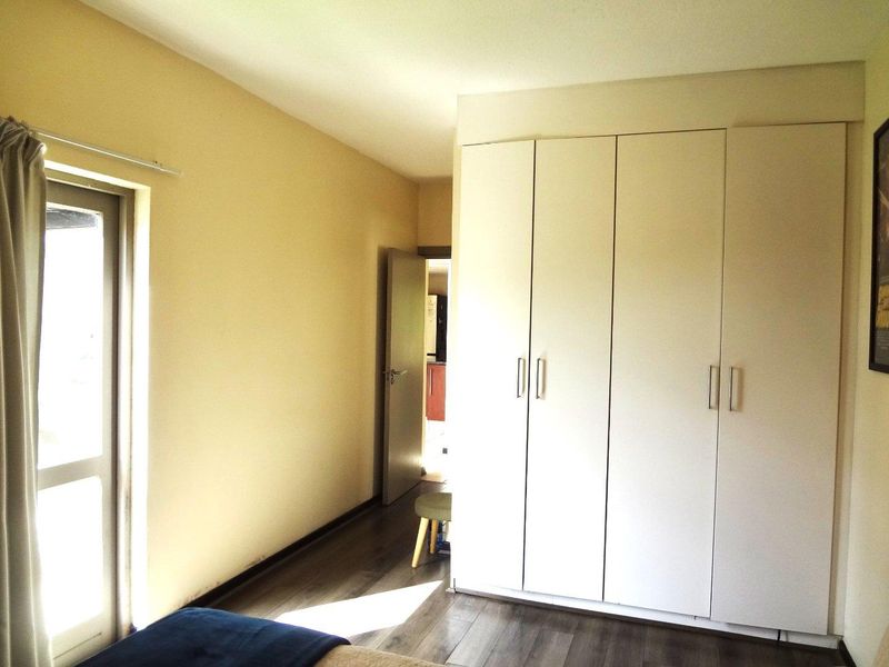 A bedroom featuring modern laminate flooring, built-in white cupboards, and a sliding door providing natural light.