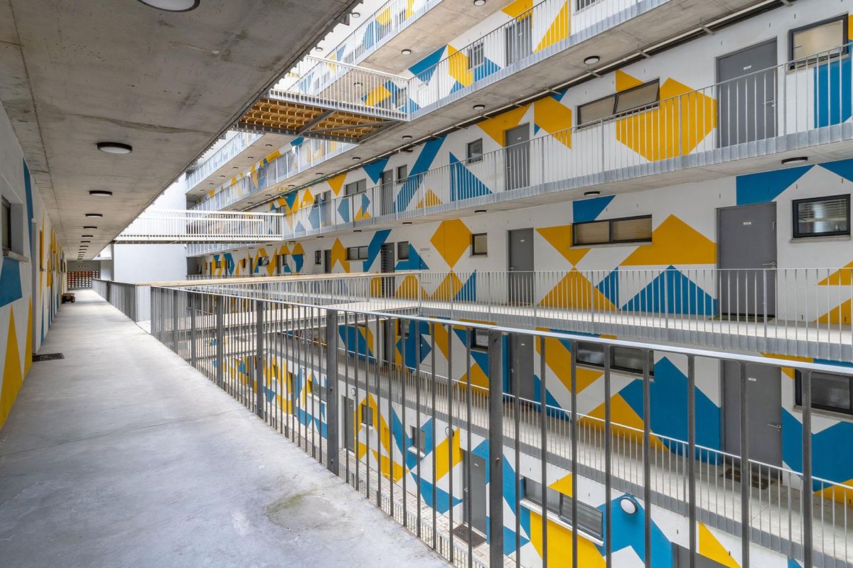 An exterior view of an apartment complex featuring open-air walkways, metal railings, and a vibrant geometric mural on the building facade.