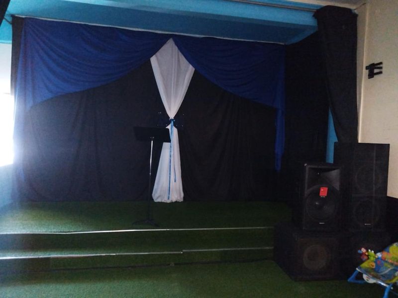 A small indoor stage area featuring a raised platform with artificial turf flooring and decorative fabric backdrop curtains.