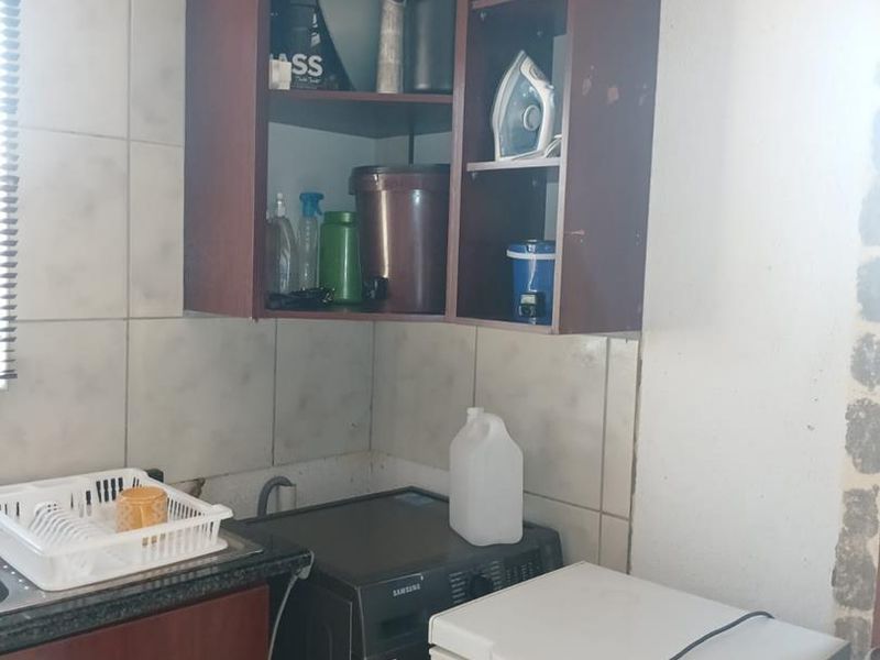 A compact laundry area featuring built-in dark wood cabinetry, tiled splashbacks, and a functional sink setup.