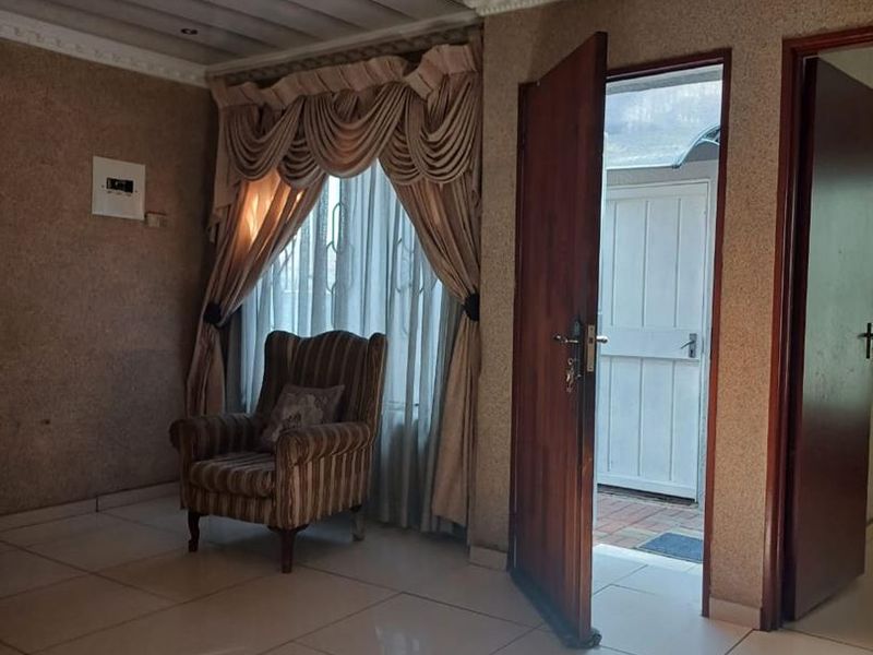 A living area featuring tiled flooring, textured walls, and decorative ceiling molding, with direct access to an exterior space through a timber door.