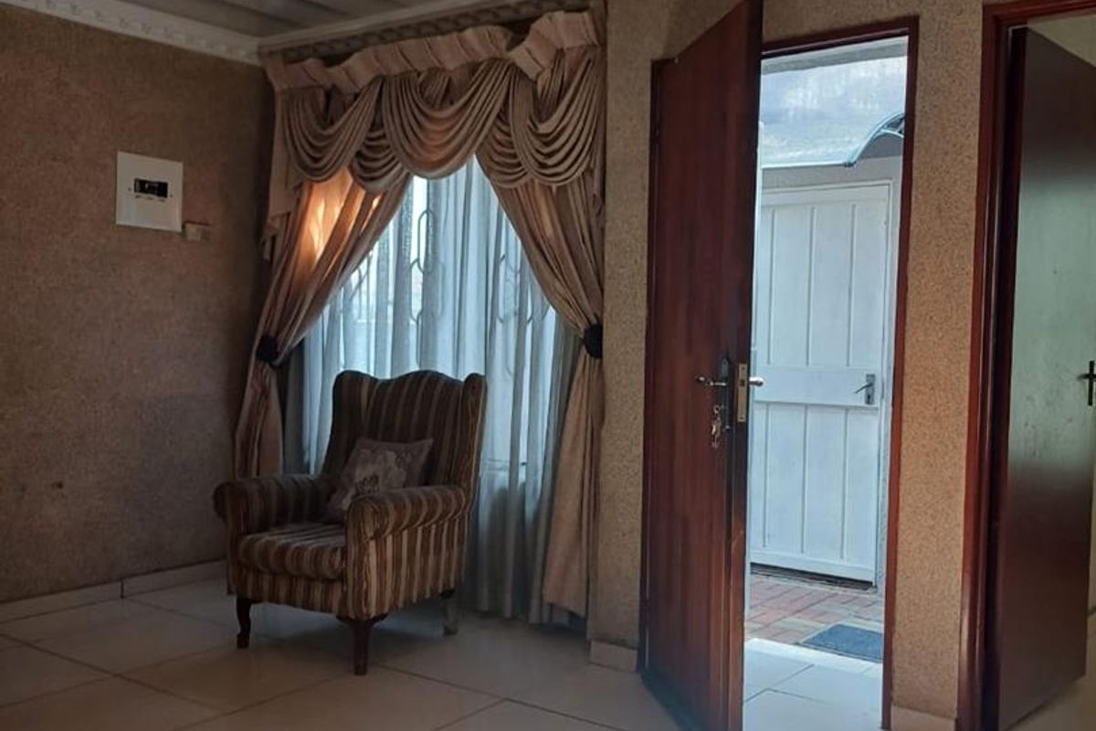 A living area featuring tiled flooring, textured walls, and decorative ceiling molding, with direct access to an exterior space through a timber door.