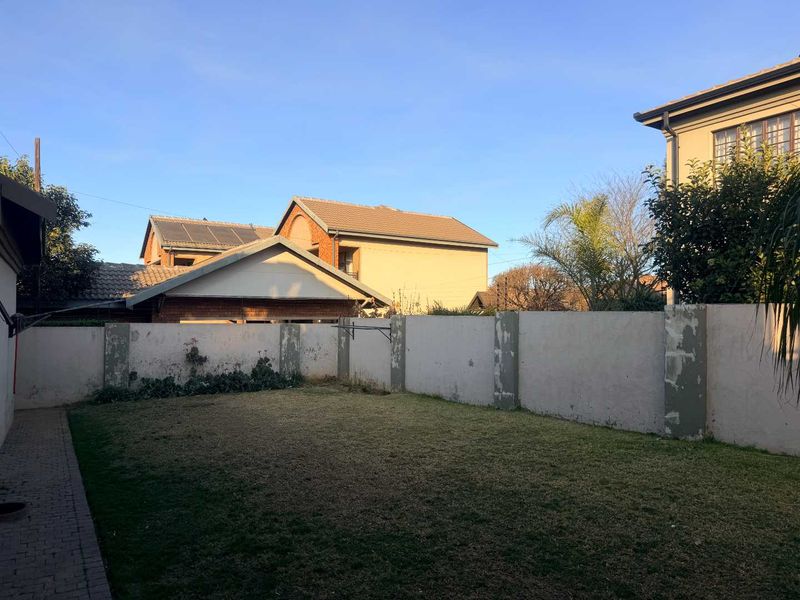 A private rear garden featuring a lawn area, paved walkway, and perimeter boundary walls showing signs of wear.
