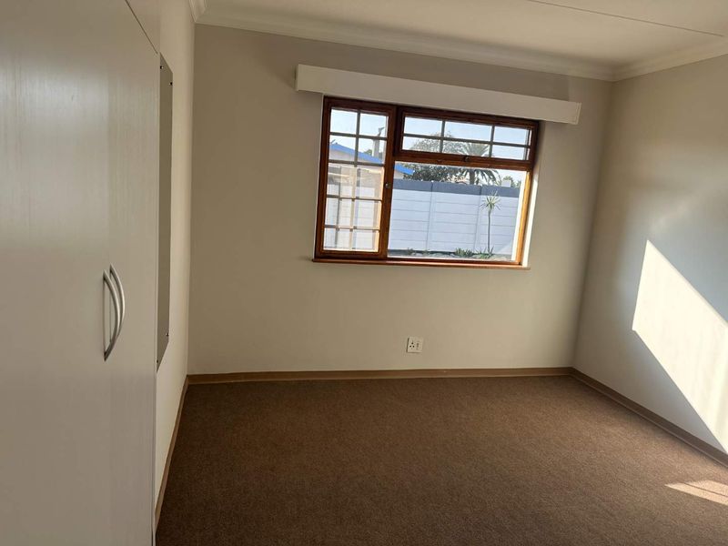 A clean, empty bedroom featuring neutral walls, carpet flooring, and a built-in wardrobe with a timber-framed window providing natural light.