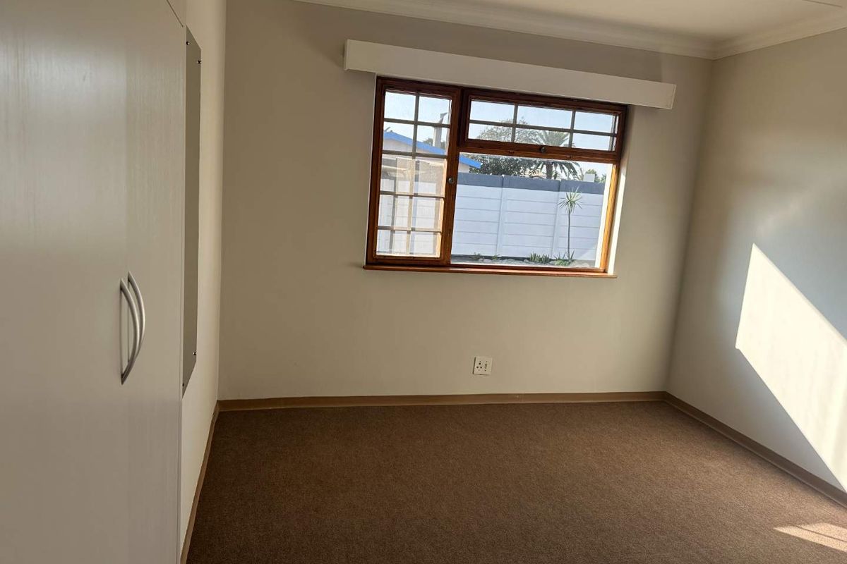 A clean, empty bedroom featuring neutral walls, carpet flooring, and a built-in wardrobe with a timber-framed window providing natural light.