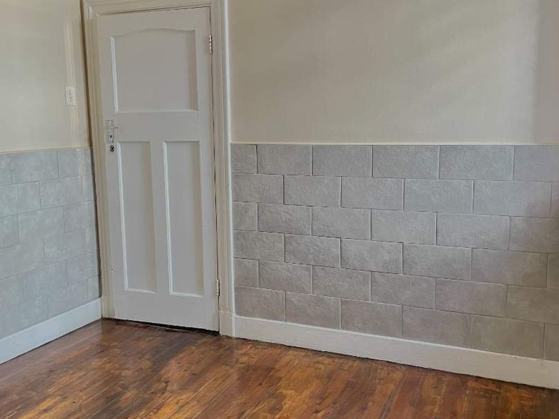 An empty bedroom featuring polished timber flooring, a classic panelled door, and decorative wainscoting along the lower walls.