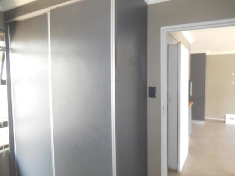 A bedroom interior featuring a large built-in wardrobe with sliding doors, leading into an adjacent living space.