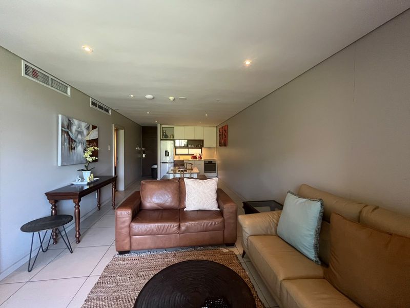 An open-plan living and kitchen area featuring tiled floors, recessed lighting, ducted air conditioning, and a functional kitchen with built-in cabinetry and appliances.