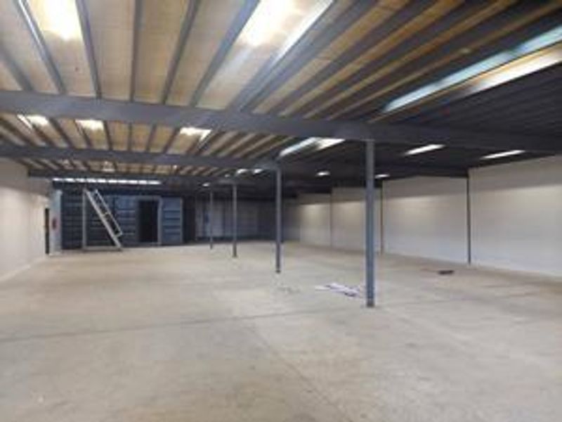 Spacious industrial warehouse unit featuring high ceilings with exposed steel beams, concrete flooring, and a mezzanine level with integrated metal staircase access.