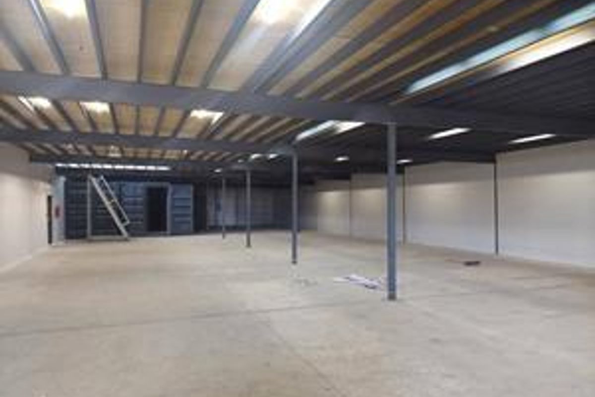 Spacious industrial warehouse unit featuring high ceilings with exposed steel beams, concrete flooring, and a mezzanine level with integrated metal staircase access.