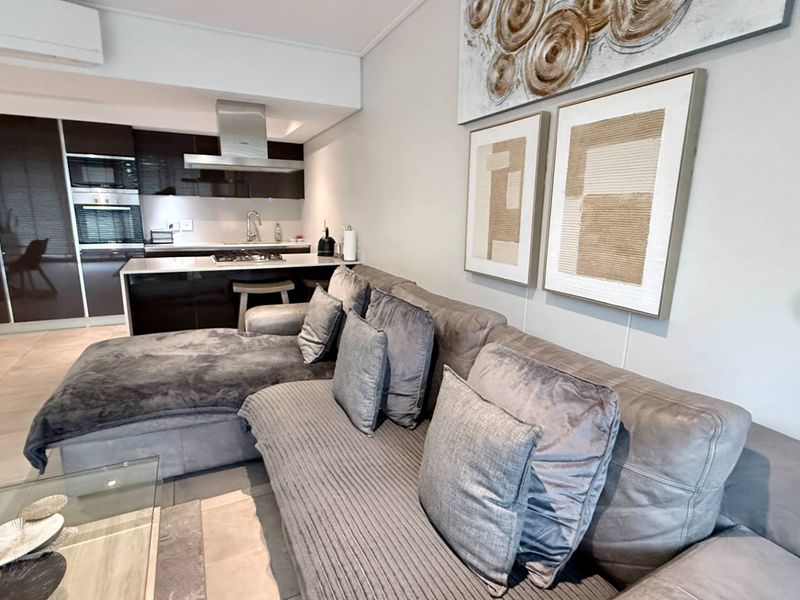 Modern open-plan living area featuring a sleek kitchen with built-in appliances, stone countertops, and neutral tiled flooring throughout.