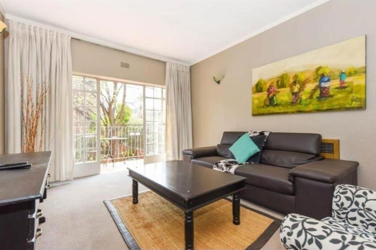 A comfortable living room featuring neutral walls, carpeted flooring, and large sliding glass doors that provide natural light and access to a private balcony.