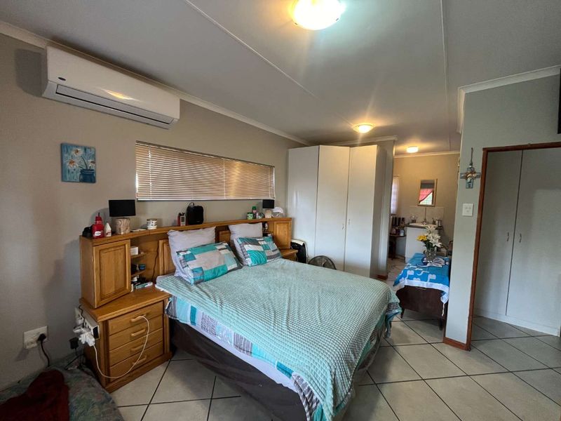 A functional bedroom featuring tiled flooring, built-in cupboards, and a wall-mounted air conditioning unit, with an adjoining small vanity or utility area.