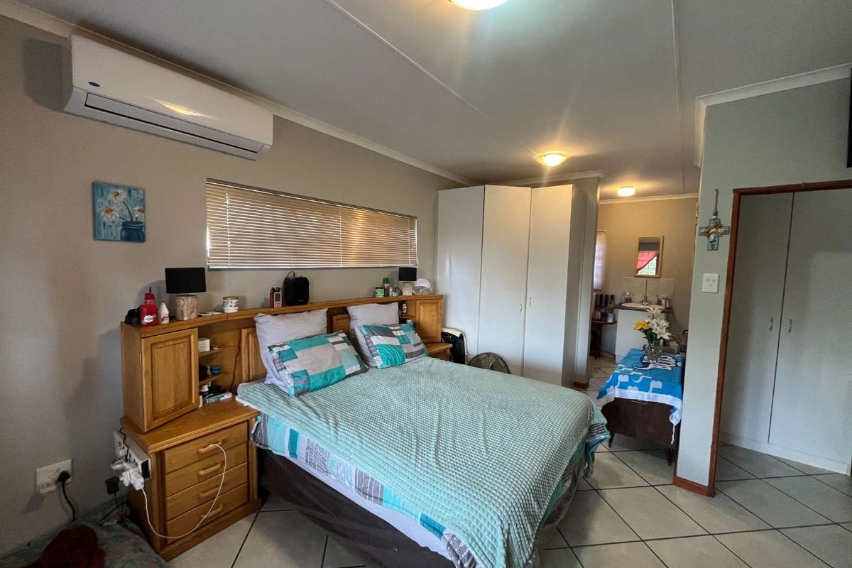 A functional bedroom featuring tiled flooring, built-in cupboards, and a wall-mounted air conditioning unit, with an adjoining small vanity or utility area.